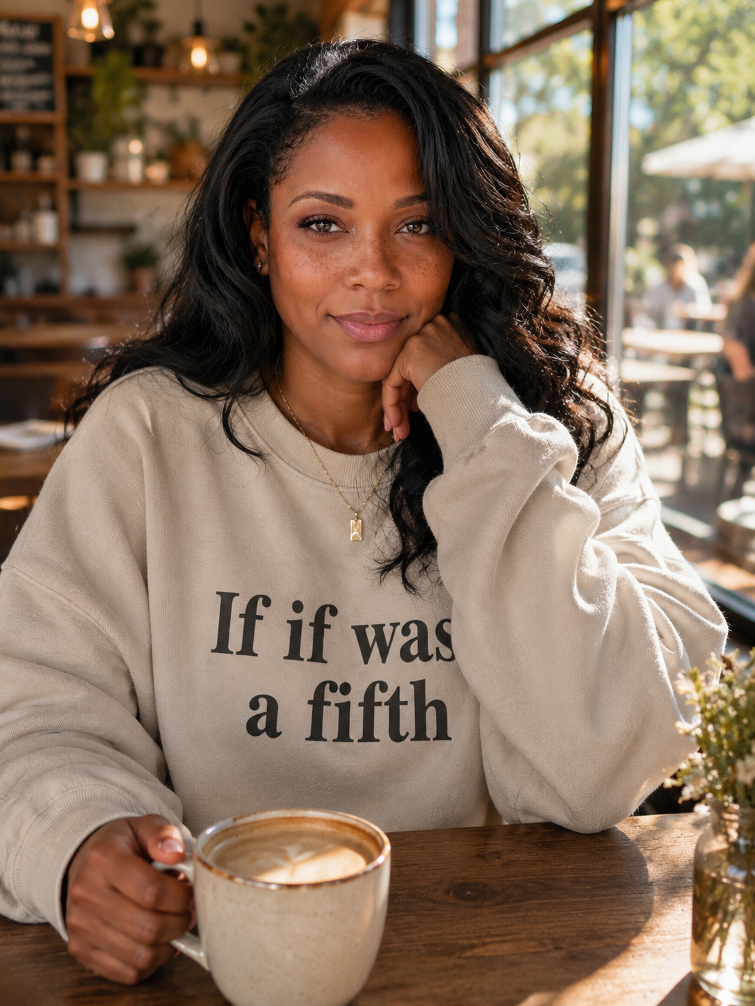 A woman in a cream hoodie holding a warm mug beside an open journal in soft morning light